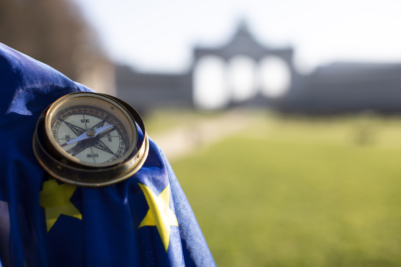 Das Foto zeigt eine EU Flagge, auf der ein Kompass liegt und im Hintergrund eine grüne Wiese.
