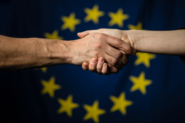 Händeschütteln vor einer Europaflagge.