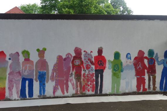 Die bemalte Wand zeigt verschiedene Menschen, bunt ausgemalt.
