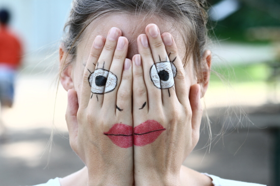 Eine Frau verdeckt ihr Gesicht mit Händen. Auf ihren Händen ist ein anderes Gesicht gemalt.