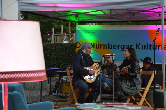 Ein Mann und eine Frau sitzen mit Gitarren in der Hand auf Klappstühlen im Freien und musizieren