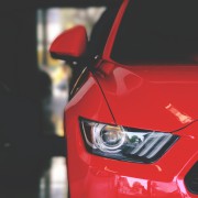 Detailaufnahme eines roten Autos. Man sieht die Front rechts vorne mit Scheinwerfer und Seitenspiegel.