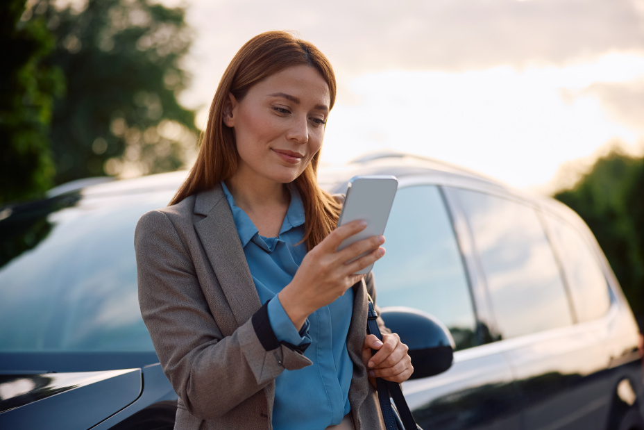 Smiling woman texting on mobile phone after driving a car.