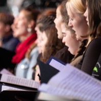 Frauen in einem Chor stehen nebeneinander, singen und halten Notenblätter vor ihrem Körper.