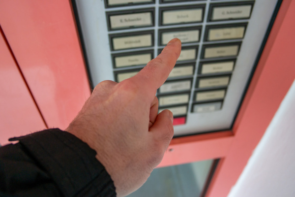 Ein Mann klingelt an der Haustür eines Mehrfamilienhauses.