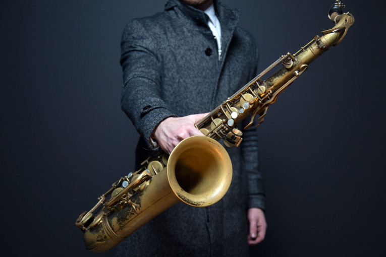 Ein Saxophon in der Hand eines Mannes mit grauem Mantel.