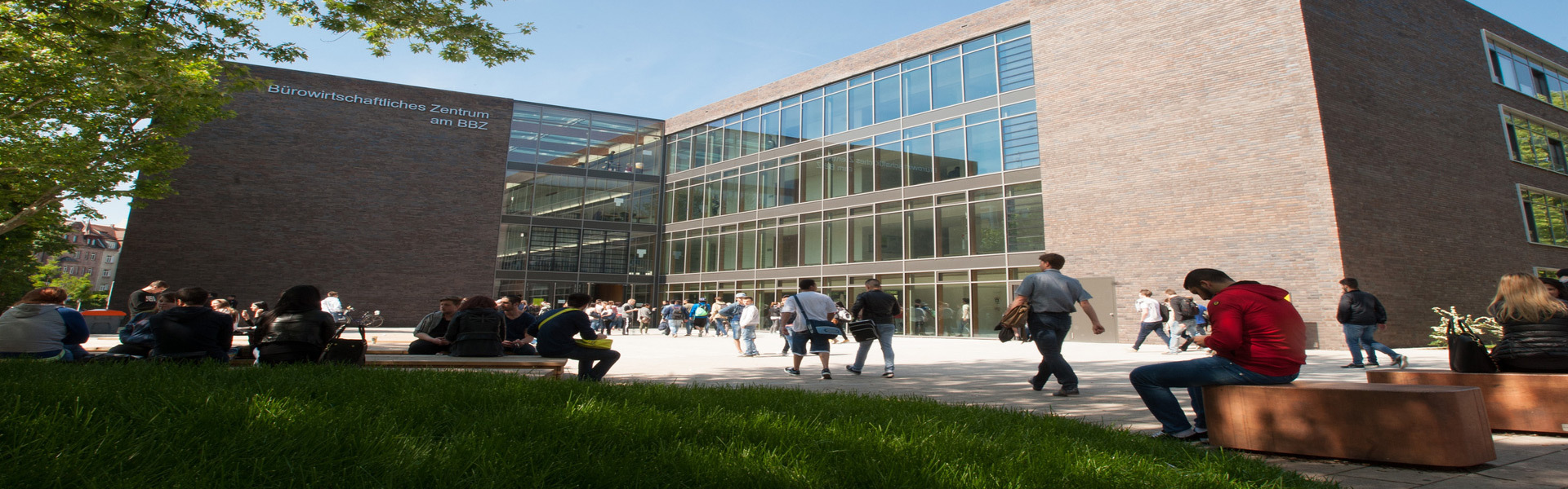 Blick auf die Berufsschule 9 im Sommer, davor Schüler auf Sitzsteinen