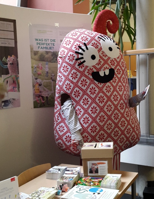 Das Maskottchen der Familienbildung Nürnberg steht an einem Infostand. © Stadt Nürnberg