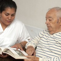 Eine Pflegerin schaut mit einem älteren Mann ein Buch an.