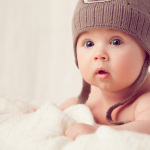 Baby lying on a soft bed cover with cap.