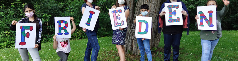 Sieben Schüler*innen halten jeweils einen Plakat mit Buchstaben des Wortes "Frieden"