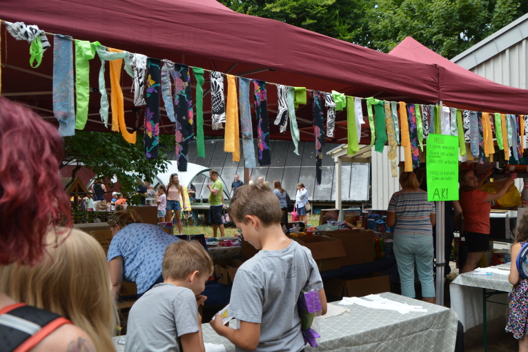 Ein Stand mit einem roten Dach und vielen bunten Wimpeln wird von Kindern umringt