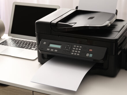 Das Bild zeigt einen Schreib·tisch mit einem Laptop und einem Drucker.
