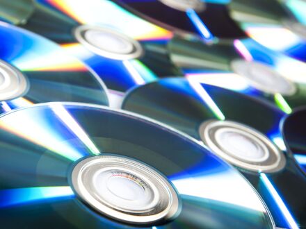 Auf dem Bild sind viele CDs. Die CDs liegen zum Teil übereinander. Die Rückseite von den CDs zeigt nach oben.
