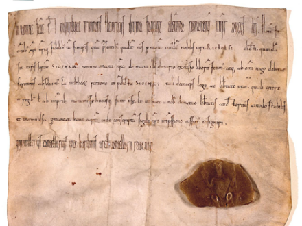 Auf dem Bild sieht man die Sigena-Urkunde. Die Urkunde ist aus altem Papier. Der Text auf der Urkunde ist mit der Hand geschrieben. Rechts unten auf der Urkunde ist ein braunes Siegel aus Wachs.