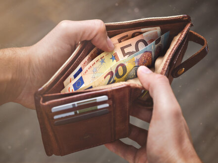 Das Bild zeigt 2 Hände von einer Person. Die Person hält einen offenen GeldÀbeutel in der Hand. In dem Geld·beutel sind Euro-Scheine.