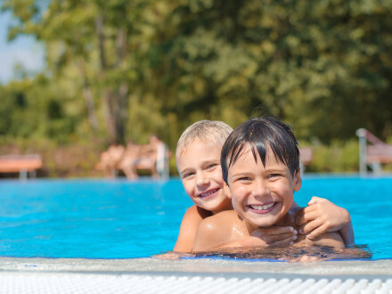 Das Bild zeigt 2 Kinder in einem Frei·bad. Die Kinder lachen.