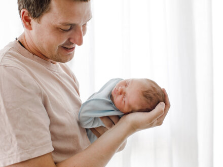 Das Bild zeigt einen Vater mit dem neu·geborenen Baby auf dem Arm.