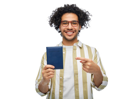 Das Bild zeigt einen jungen Mann mit einem Pass in der rechten Hand. Mit der linken Hand deutet der Mann auf den Pass. Der Mann lächelt.