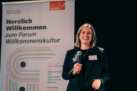 Katharina Schwartz mit Mikrofon in der Hand, im Hintergrund ein Roll-Up