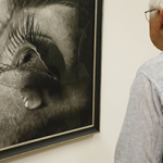 Ein Mann betrachtet das gerahmte Foto einer Nahaufnahme eines weiblichen Auges an einer Wand