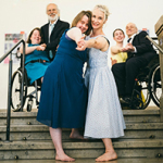 Mehrere Personen, teils in Rollstuhl, tanzen auf einer Treppe