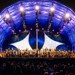 Ein Orchester steht auf einer bunt beleuchteten Konzertbühne beim Klassik Open Air.