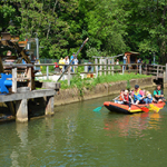 Mehrere Personen fahren auf einem Schlauchboot die Pegnitz entlang. Links im Bild ist ein Wassermühlenrad zu sehen