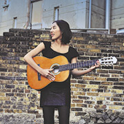 Eine Frau steht mit einer Gitarre in der Hand vor einer Mauer