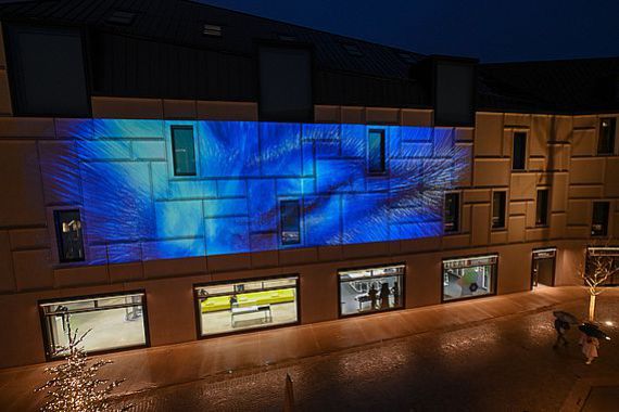 Blick von oben gegenüber auf die langgestreckte Fassade des Zukunftsmuseums mit der blauen Projektion Heaven