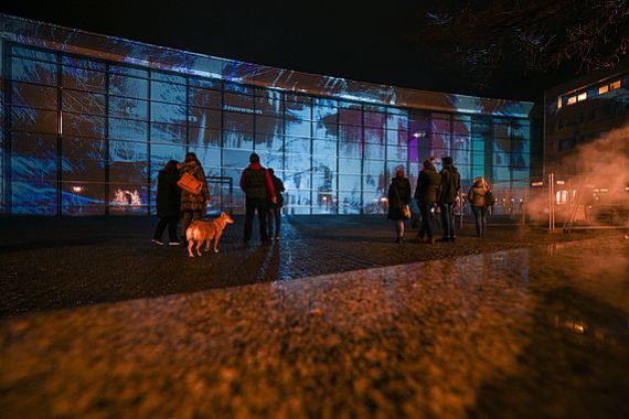 Menschengruppen stehen nachts auf dem Klarissenplatz und schauen sich die Projektion von Philipp Geist an.