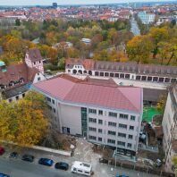 Auf der gesamten Dachfläche des Schulneubaus in der Reutersbrunnenstraße 14 sind rote Indach-Photovoltaikmodule verbaut, um diese farblich in die umgebene Dachlandschaft einzuordnen.