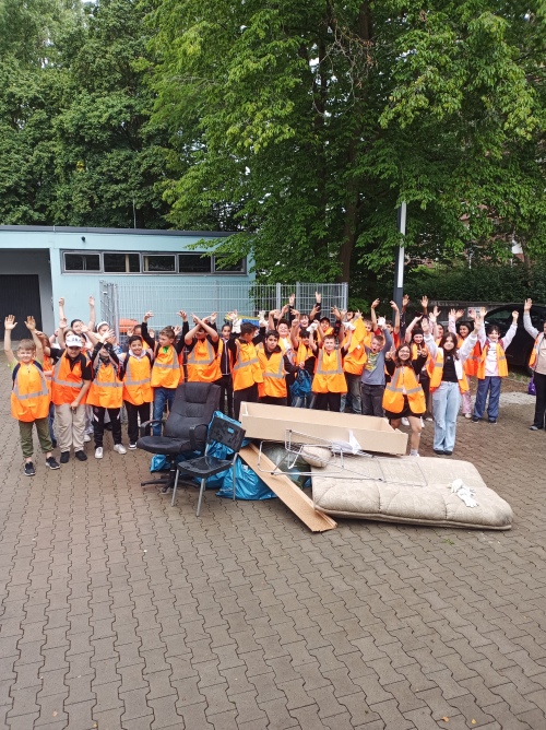Die Kinder der Mittelschule am Neptunweg haben ihre Hände in die Luft gestreckt und freuen sich über ihren gesammelten Müll, der vor ihnen liegt.