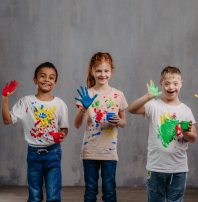 Fröhliche Kinder mit Fingerfarbentöpfchen in der Hand und bemalten Händen und T-Shirts