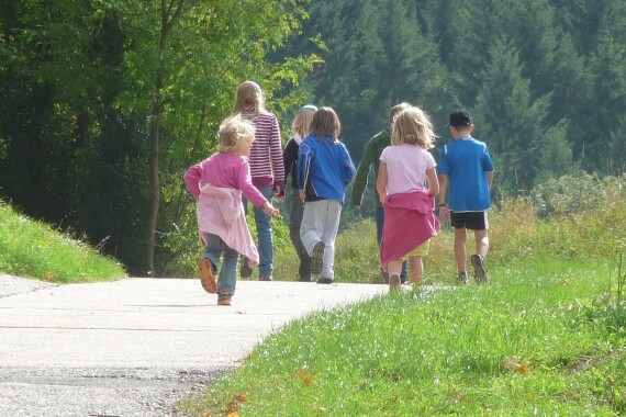 Kinder laufen auf einem Weg zwischen Wald und Wiese entlang