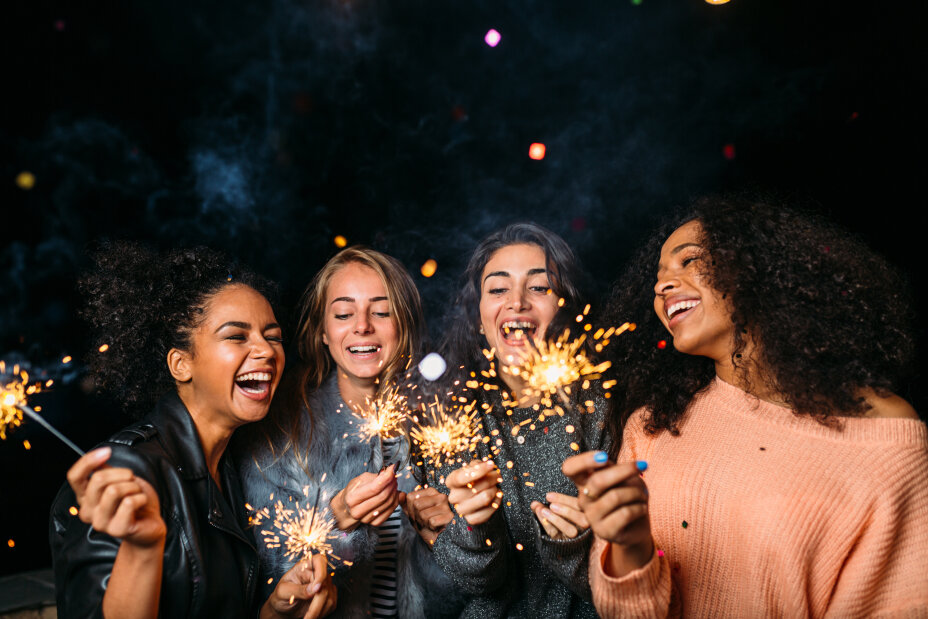 Gruppe an Silvester, hält Wunderkerzen in der Hand, lachen, dunkler Hintergrund