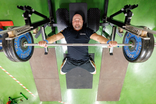 Foto: Blick von Oben auf den Kraftsportler Thomas Ziegler, der auf einer Bank liegend eine Langhantel nach oben drückt.