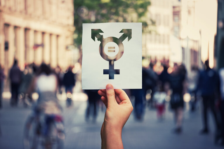 Hand hält ein Blatt mit Transgender-Symbol und Gleichheitszeichen innen.