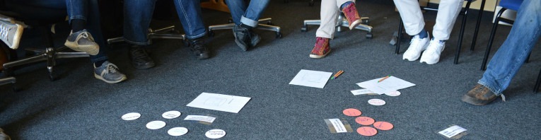Bunte, beschriftete Karten liegen auf dem Boden, um die Seminarteilnehmer in einem Stuhlkreis sitzen.