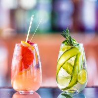 Zwei sommerlich anmutende, farbenfrohe Cocktails auf einer Theke.