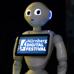 Ein Roboter aus weißem Plastik hat auf seiner Brust ein Tablet montiert. Eingeblendet ist der Schriftzug "Nürnberg Digital Festival".