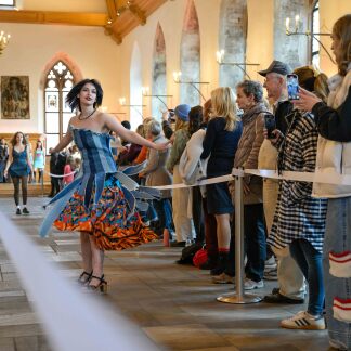 ( Bild: Anestis Aslanidis ) Eine Frau läuft einen Laufsteg im historischen Rathaussaal entlang und präsentiert ein orange-blaues Kleid auf einer Modenschau der Modeschüler.