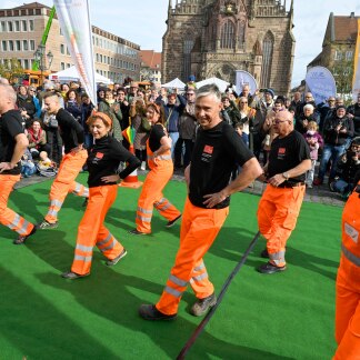 ( Bild: Anestis Aslanidis / Anestis Aslanidis ) Sör-Ballett: Mitarbeitende von Sör, in orange gekleidet, führen auf dem Hauptmarkt einen Tanz auf.
