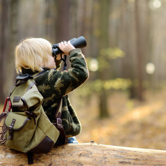 ( Bild: Maria Sbytova ) Kleiner Junge mit einem Fernglas im Wald.