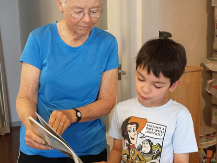 Das Bild zeigt eine ältere Frau mit einem Jungen. Die Frau zeigt dem Jungen etwas in einem Buch.