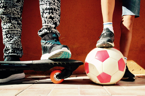Zwei Kinder mit einem Skateboard und einem Fußball.