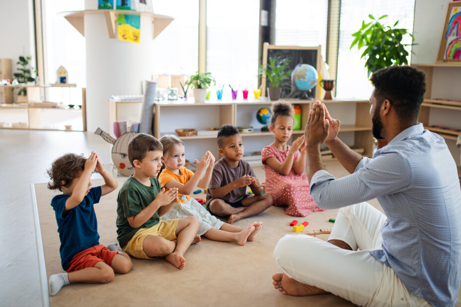 Bild © AdobeStock A group of small nursery school children with man teacher sitting on floor indoors in classroom, playing., Bild © AdobeStock