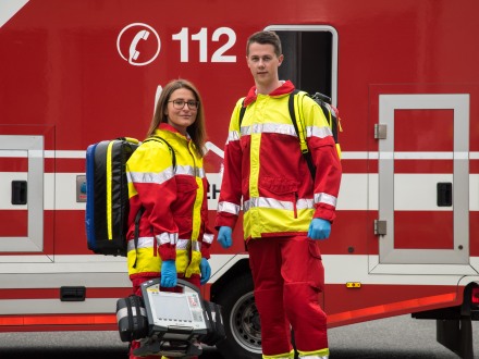 Das Bild zeigt 2 Not·fall·sanitäter vor einem Feuerwehr·auto.