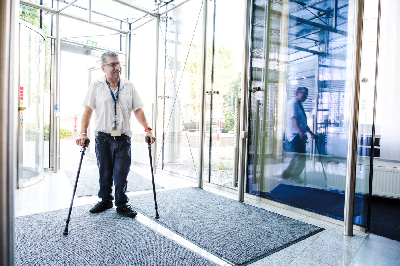 Bild © Andi Weiland / gesellschaftsbilder.de Mann mit Krücken betritt Gebäude durch Glastür, Bild © Andi Weiland / gesellschaftsbilder.de
