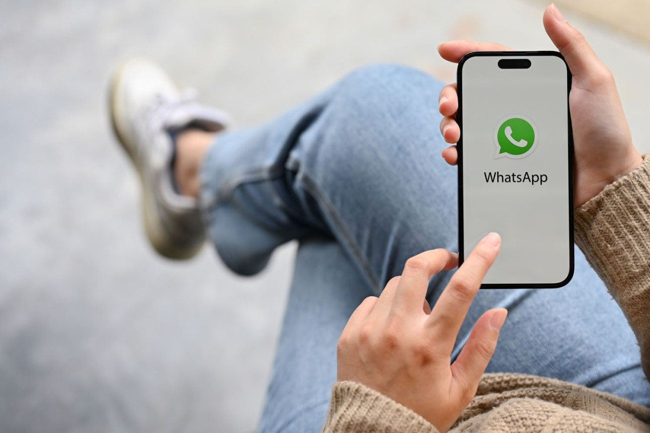 Bild © Bongkarn / AdobeStock Eine junge Frau schaut auf das Display ihres Handys. Darauf ist das WhatsApp Logo zu sehen., Bild © Bongkarn / AdobeStock